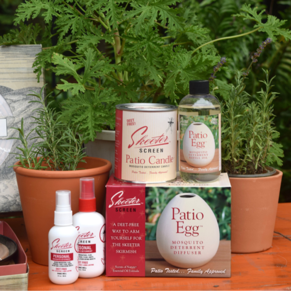 A display of Skeeter Screen mosquito deterrent products, including a patio candle, Patio Egg diffuser, spray bottles, and diffuser oil, arranged on a wooden table with potted plants and greenery in the background.