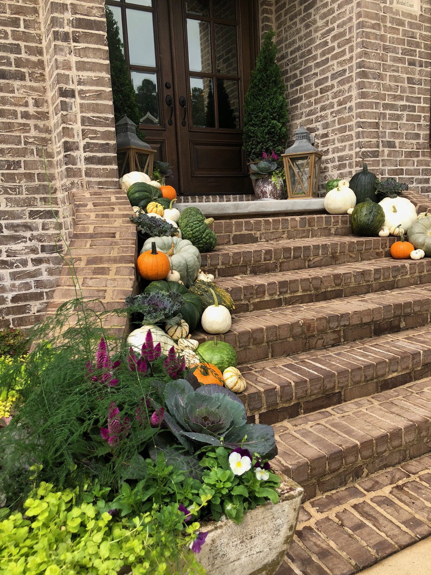Brick front steps decorated with various pumpkins, gourds, and potted ornamental kale and flowers.